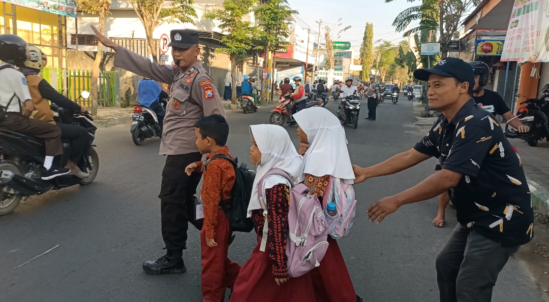 BERTARUH NYAWA: Seorang polisi membantu siswa menyeberang jalN. (Khoyrul Umam Syarif/Kabar Madura)